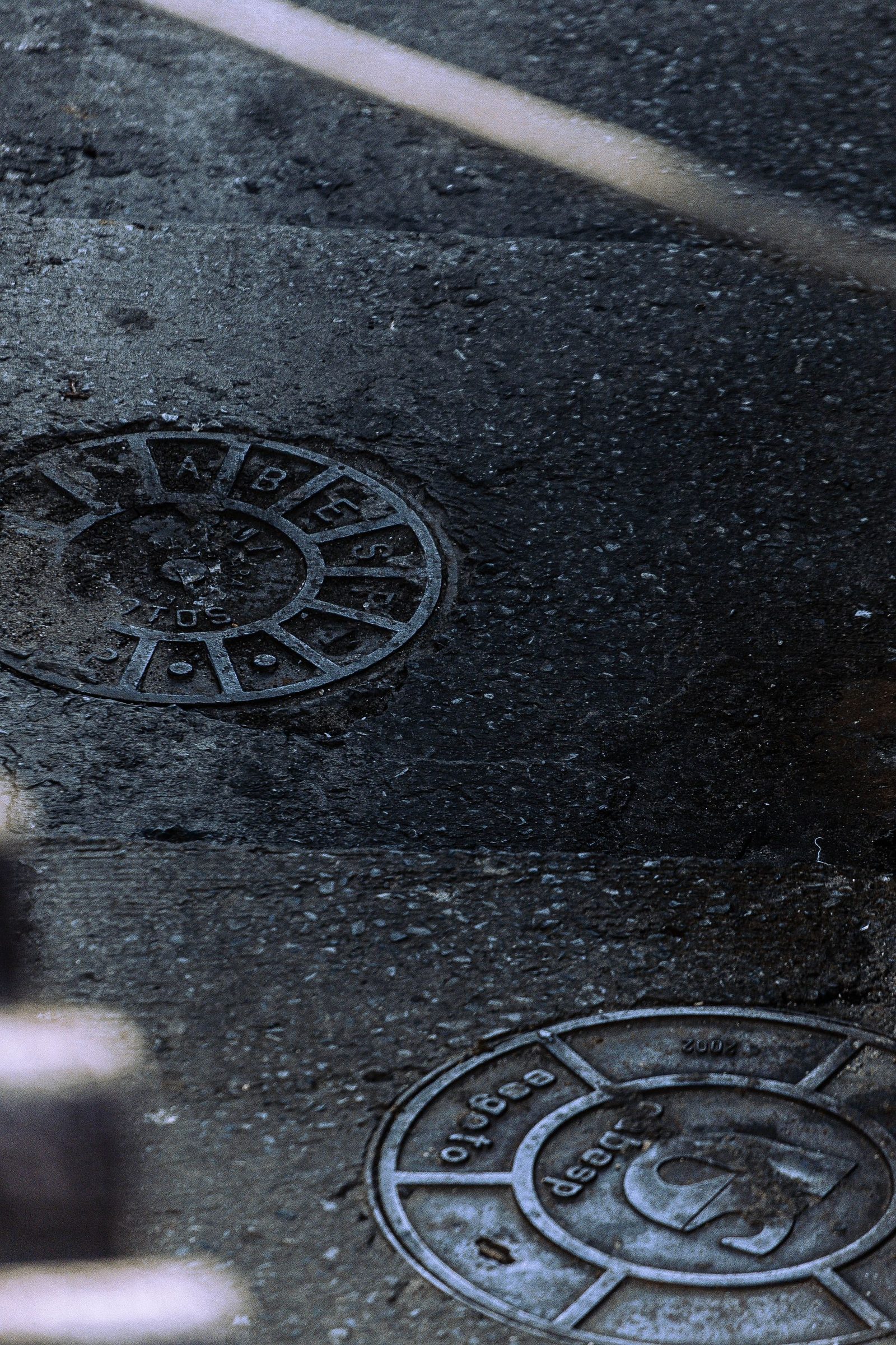 Two cast iron manhole covers set into a wet street surface
